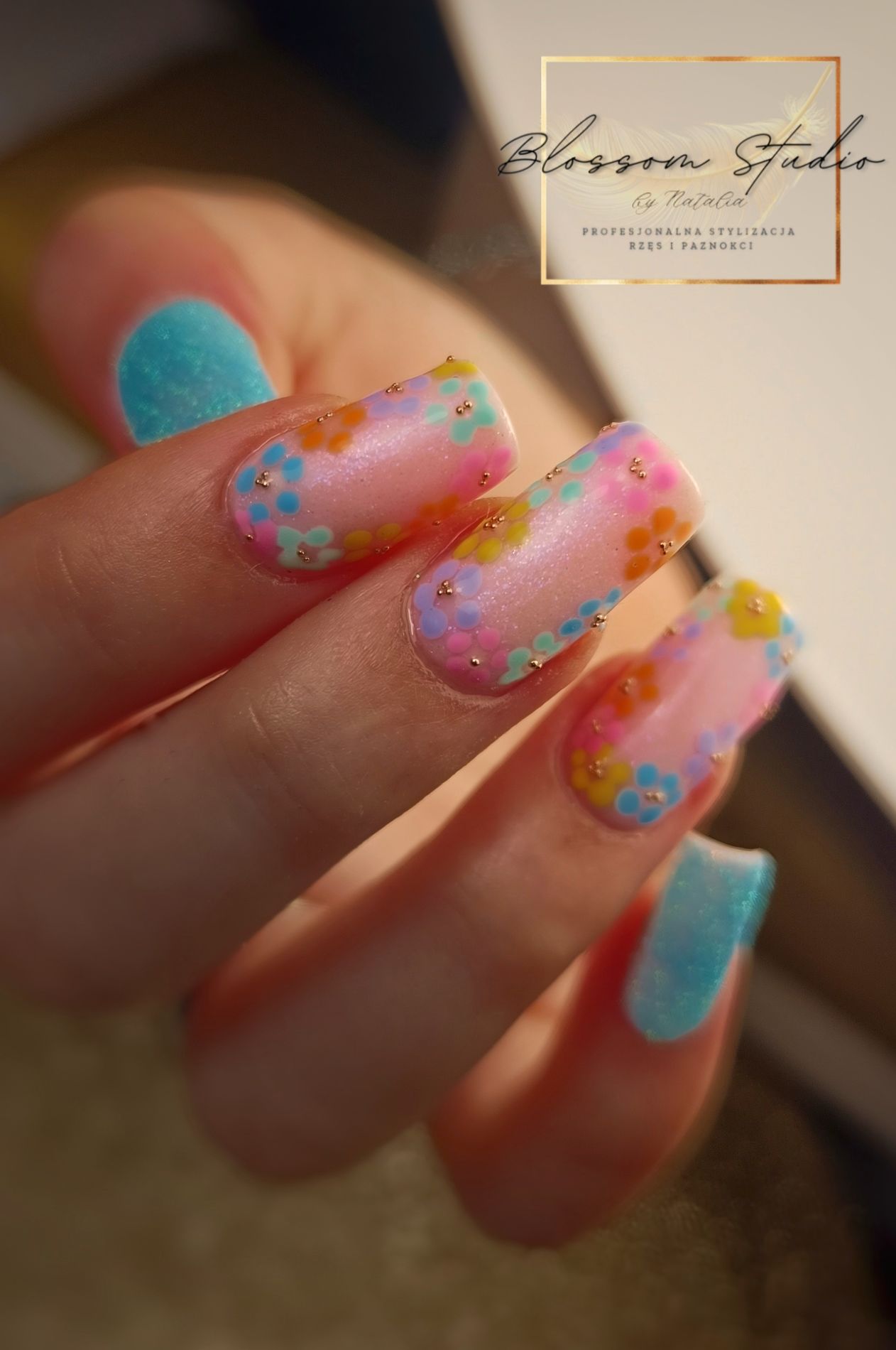 Vierkante nagels met handgeschilderde pastelbloemetjes, met het logo van Blossom Studio