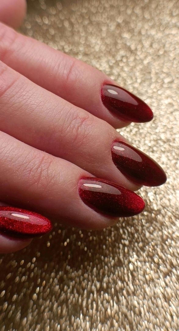 Diep rode glitternagels in amandelvorm op een gouden ondergrond